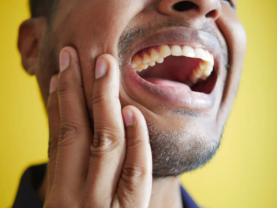 Homem com a mão na face e a boca aberta, em sinal de dor na mandíbula
